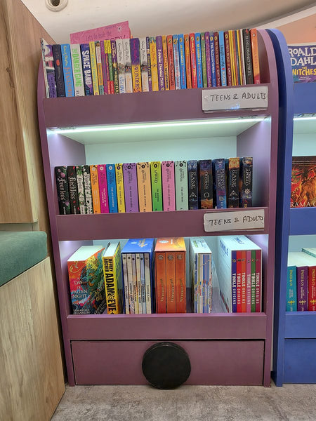 Fully stocked purple bookshelf of chapter books for teens and adults at Brain Chapters
